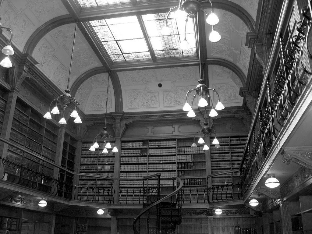 Biblioteca jurídica de techos altos con estanterías de madera y lámparas colgantes